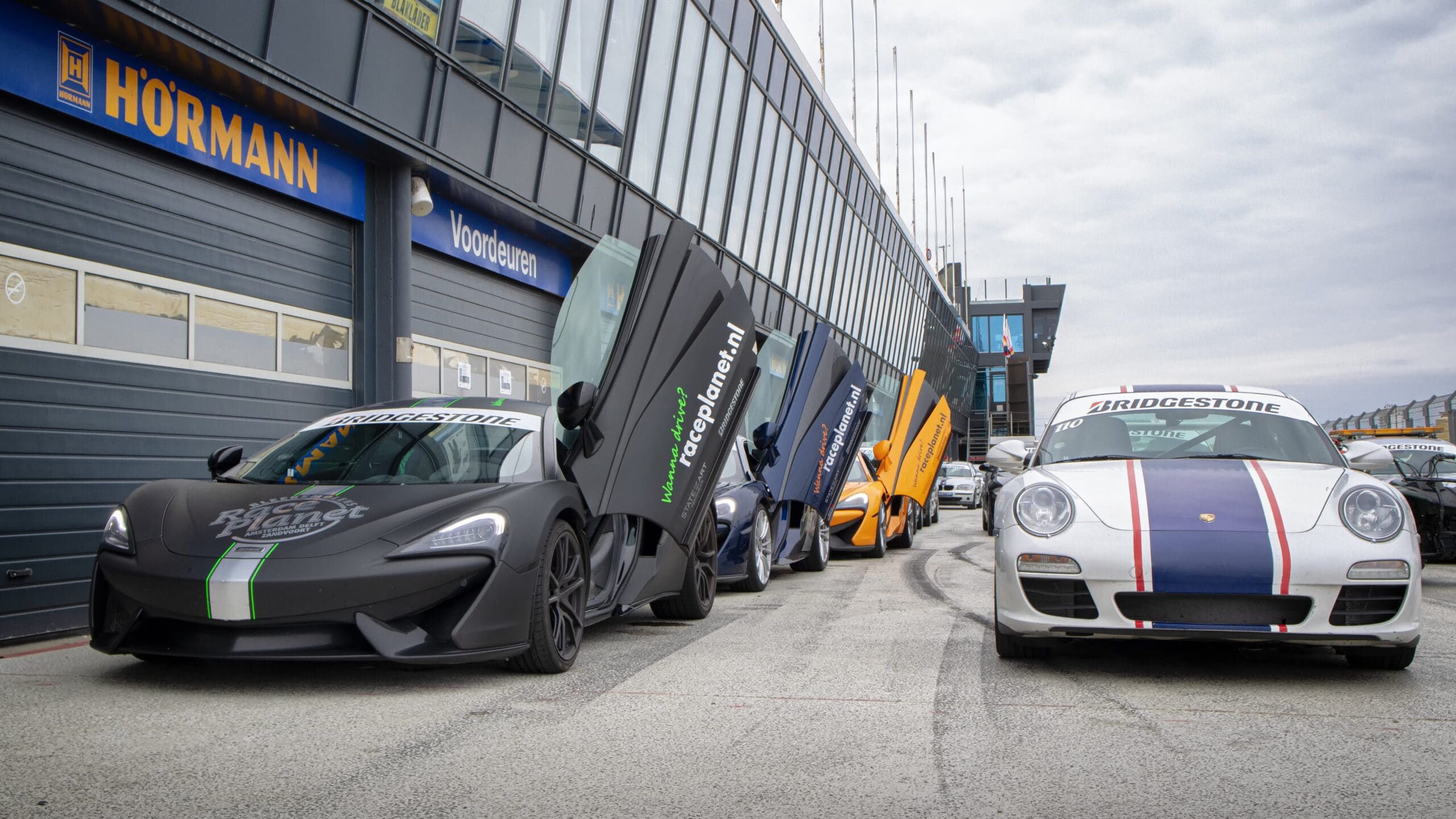 Supercars met McLaren 540c en Porsche 911 staan klaar in de pitstraat van Circuit Zandvoort bij een Race Planet.